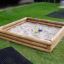 Holz-Sandkasten im Garten mit Spielzeug-Schaufeln.