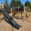 Holzspielplatz mit Rutsche und Klettergerüsten im Freien.