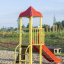 Grashüpfer Spielturm mit Rutsche und rotem Dach auf einem Spielplatz.