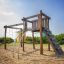 Kampinos Klettergerüst mit Kletternetz und Rutsche auf einem sandigen Spielplatz.