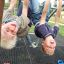 Zwei Kinder hängen lachend kopfüber an einer Kletterstange auf einem Spielplatz.