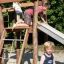 Kinder spielen auf einem hölzernen Spielgerät Bergila Spielkombination mit Rutsche im Freien.