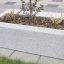 Blumentopf Milano aus Beton mit jungen Pflanzen auf gepflasterter Oberfläche.