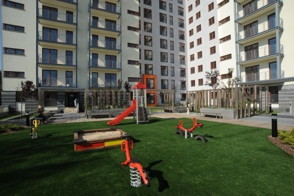 Spielplatz mit Kunstrasen im Hof eines modernen Wohngebäudes, ausgestattet mit Rutsche und Federspie