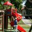 Kinder spielen auf einem Spielplatz mit Lars Laj Kunstrasen 70 und roter Rutsche.