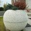 Grauer Blumentopf Globe mit Zierpflanzen vor einem Haus.
