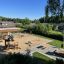 Villa Spielhaus mit Sandkasten und Rutsche auf einem sonnigen Spielplatz.