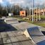 Außenansicht eines Skateparks mit Rampen und Spielplatz im Hintergrund.