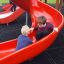 Zwei Kinder spielen auf einer roten Rutsche der Berlin Spielanlage mit Spielturm.