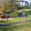 Spielplatz mit Informationstafel und roter Rutsche in einem Park.