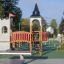 Freistehende Betontischtennisplatte auf einem Spielplatz neben einem hölzernen Spielgerüst.