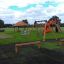 Doppelter Schaukel Rahmen auf einem Kinderspielplatz mit Rutsche und Klettergerüst.