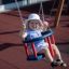 Kleines Mädchen lächelt auf der Schaukel Rahmen (Doppelt) auf dem Spielplatz.