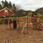 Spielplatzgerät Panther Kletteranlage auf einem Sandplatz mit roten Häusern im Hintergrund.