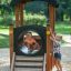 Zwei Kinder spielen mit einem Lokomotive Spielhaus auf einem Spielplatz.