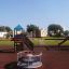 Kinderspielplatz mit Logo Spielturm mit Rutsche, Schaukel und Kletternetz in einem sonnigen Park.