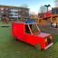 Rotes Feuerwehr LKW Spielhaus auf einem Spielplatz mit weiteren Spielgeräten im Hintergrund.