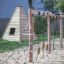 Wigwam Spielhaus aus Holz neben einem Klettergerüst mit Seilnetz auf einem Sandplatz.