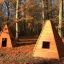 Zwei Wigwam Spielhäuser aus Holz im Herbstwald mit fallenden Blättern.