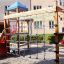 Spielturm mit Rutsche, Kletterseil und Brücke auf einem Spielplatz.