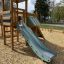 Spielkombination mit Spielturm, Kletterwand und langer Rutsche auf einem Spielplatz.