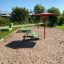 Grüne Umbrela-Wippe auf einem Spielplatz mit rotem Dach und Sandboden.