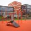 Spielplatzgerät New Age Fit MEDIUM vor modernem Schulgebäude.
