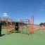 Outdoor-Fitnessgeräte aus Metall in Orange und Grau auf grünem Gummiuntergrund.