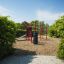Roter Spielplatz New Age Fit mit Klettergerüst und Rutsche, umgeben von grünen Hecken.
