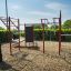 Outdoor-Fitnessgerät New Age Fit auf einem Spielplatz mit roten und schwarzen Elementen.