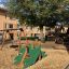 Rutsche mit Drachenschwanz auf einem Spielplatz, umgeben von anderen Spielgeräten und einem Wohngebä