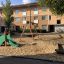 Spielplatz mit Rutsche mit Drachenschwanz und Schaukeln vor einem Wohnhaus.