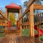 Holzspielplatz mit roter Spiralrutsche und mehreren Ebenen im Freien.