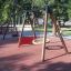 Schaukelgestell aus Holz und Metall mit roter Fallschutzplatte 55 in einem Park.
