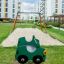 Doppelte Auto Federwippe in Grün auf einem Spielplatz mit Sandfläche und Schaukel im Hintergrund.