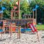 Buntes Mast Klettergerüst für Kinder auf Sandplatz mit Rutschen und Kletterseilen.