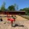 Rotes Sand Bagger Spielgerät auf einem Kinderspielplatz mit Hackschnitzeln und Bäumen im Hintergrund
