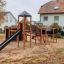 Spielturm mit Tunnel, Kletterwand und Rutsche im Garten.
