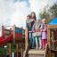 Kinder spielen auf einem großen Spielplatz mit Spieltürmen, Rutsche und Kletterwand.