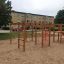 Kletteranlage mit Rutsche auf einem Spielplatz, umgeben von Sand und Bäumen.