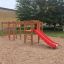Kletteranlage mit Rutsche aus Holz und roter Rutsche auf einem Sandspielplatz.