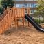 Spielturm mit Rutsche und Kletterleiter auf einem Sandboden