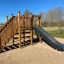 Spielturm mit Rutsche und Kletterwand im Freien auf einem Spielplatz.