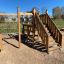 Holz-Spielturm mit Rutsche und Klettergerüst auf einem Spielplatz.