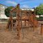 Spielturm mit Rutsche auf einem Spielplatz mit Sandboden, umgeben von Grünflächen und Gebäuden
