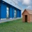 Holz-Spielhaus Natur Spielhaus auf grünem Gras vor modernem blauem Gebäude.
