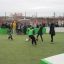 Kinder spielen Fußball in einem kleinen Fußballfeld mit grünem Kunstrasen und weißen Banden, umgeben