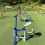 Kinder-Fitnessgeräte im Freien auf einem Spielplatz mit grünem Boden und Bäumen im Hintergrund.