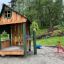 Holzspielhaus Nills Spielhaus im Freien auf einem Spielplatz, umgeben von Bäumen.