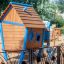 Holzspielhaus für Kinder mit Rutsche und blauen Fensterläden im Park.